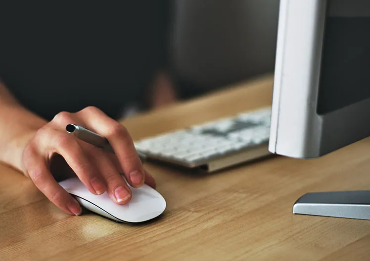 Main utilisant une souris devant un écran d’ordinateur
