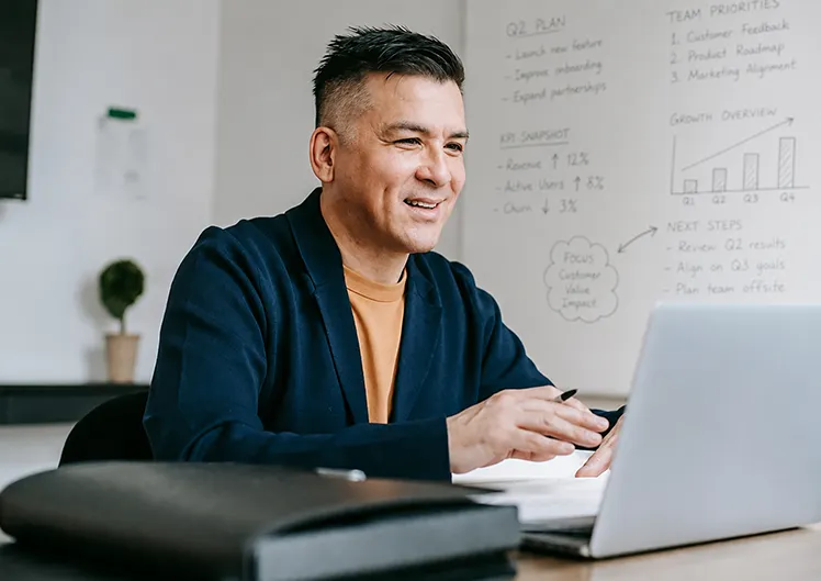 Personne travaillant sur un ordinateur portable, avec un carnet et un stylo sur le bureau